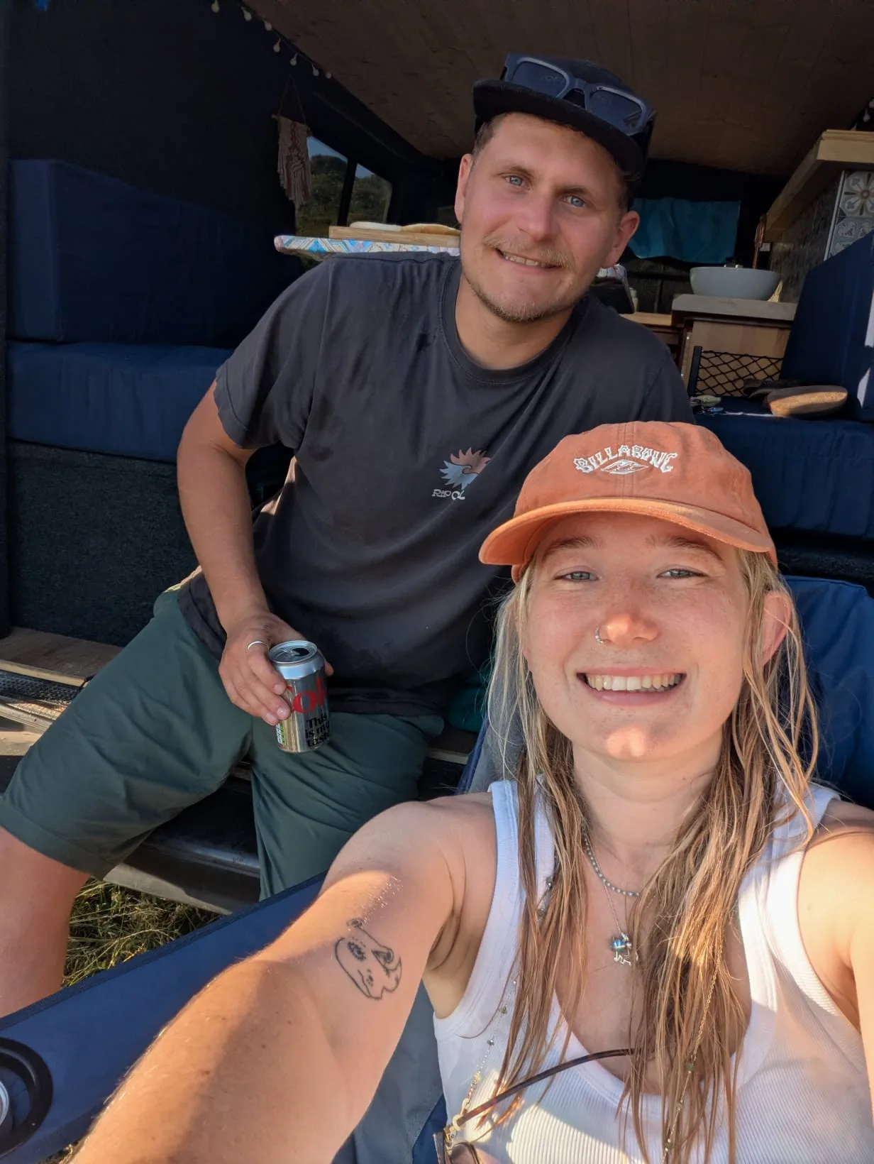 Tessa and Callum sitting in the open back of a van on a sunny day.