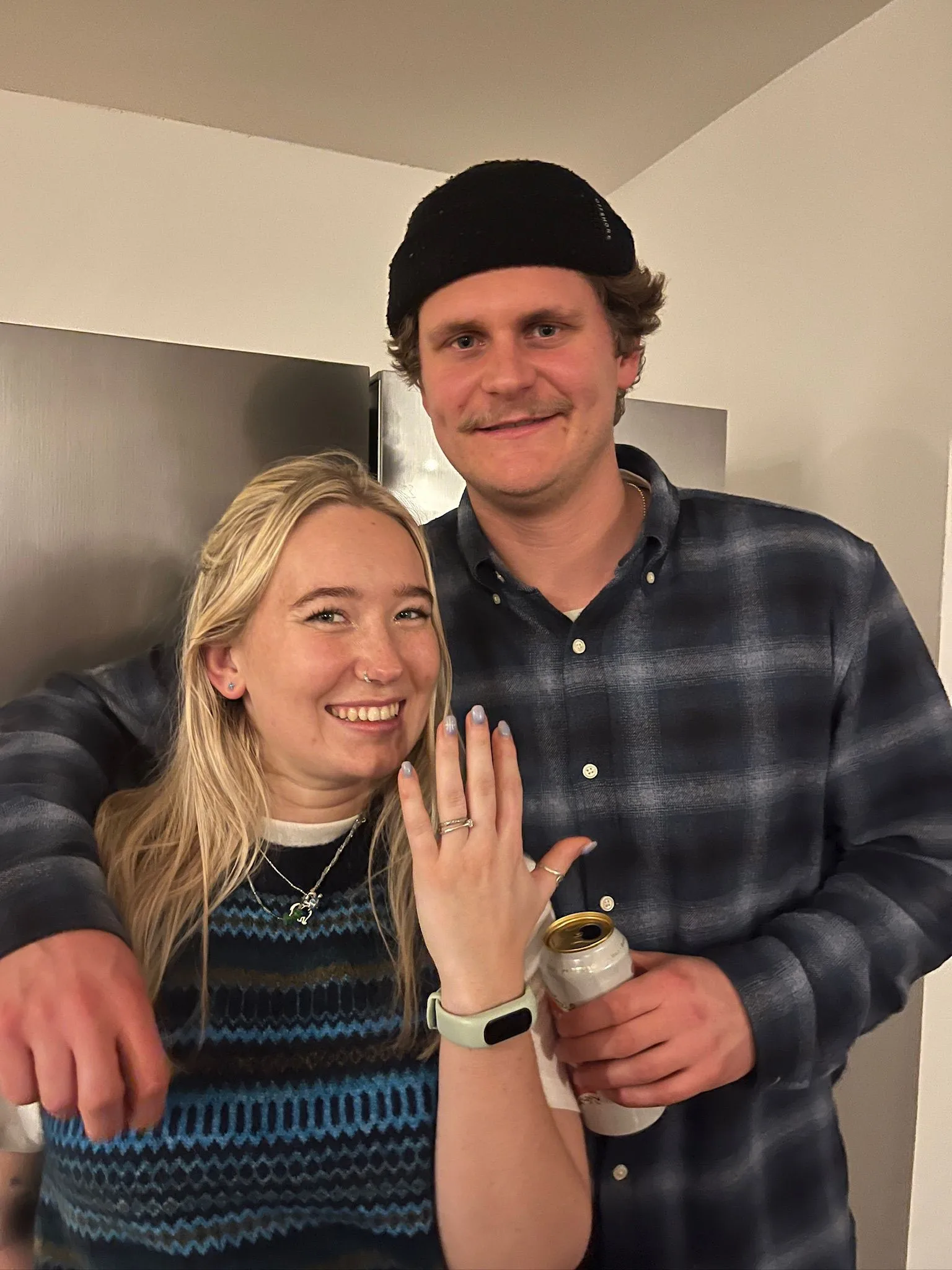 Tessa holding out her hand to show her engagement ring, with Callum beside her.