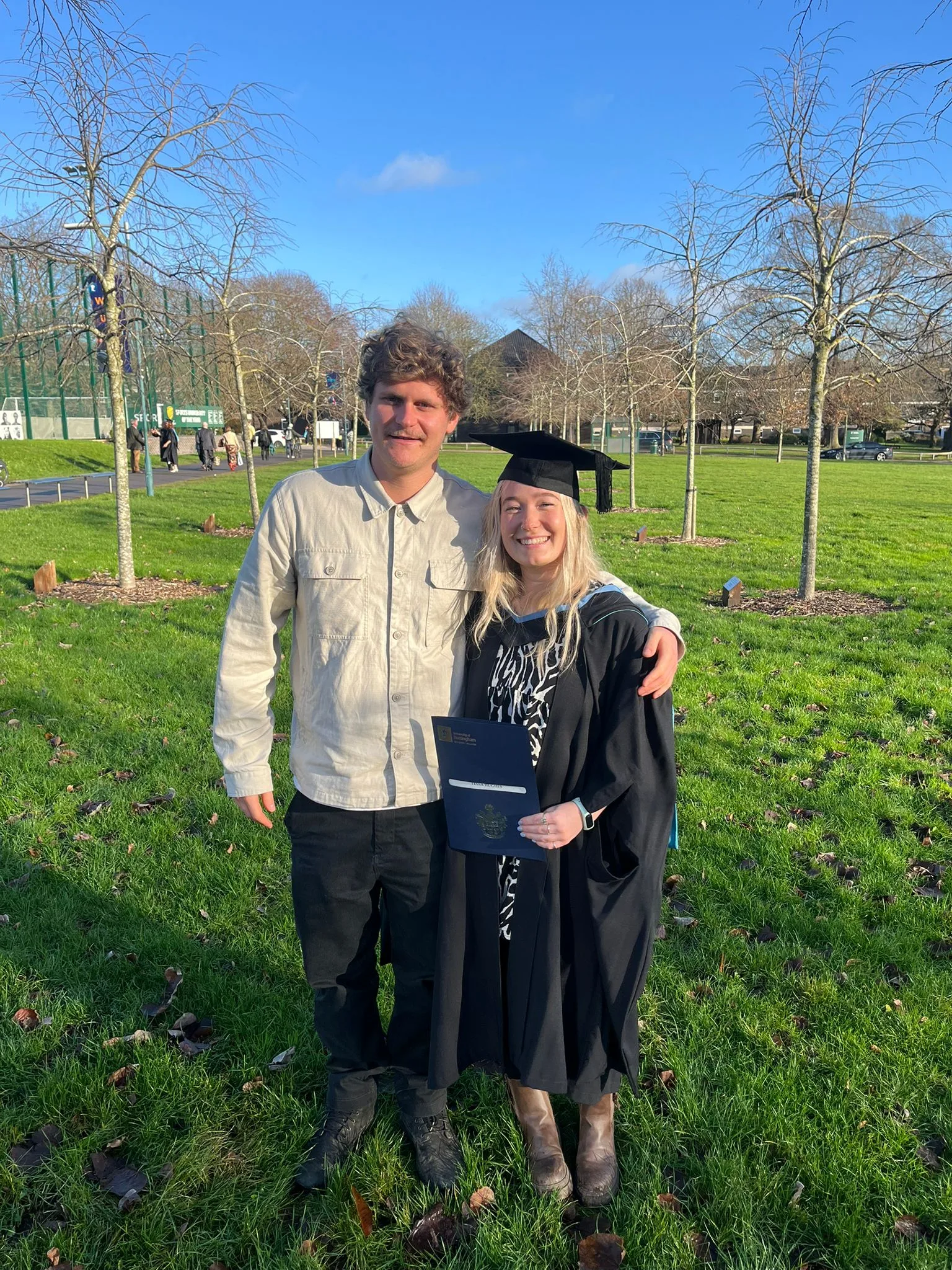 Tessa in a graduation cap and gown standing with Callum on a sunny lawn.