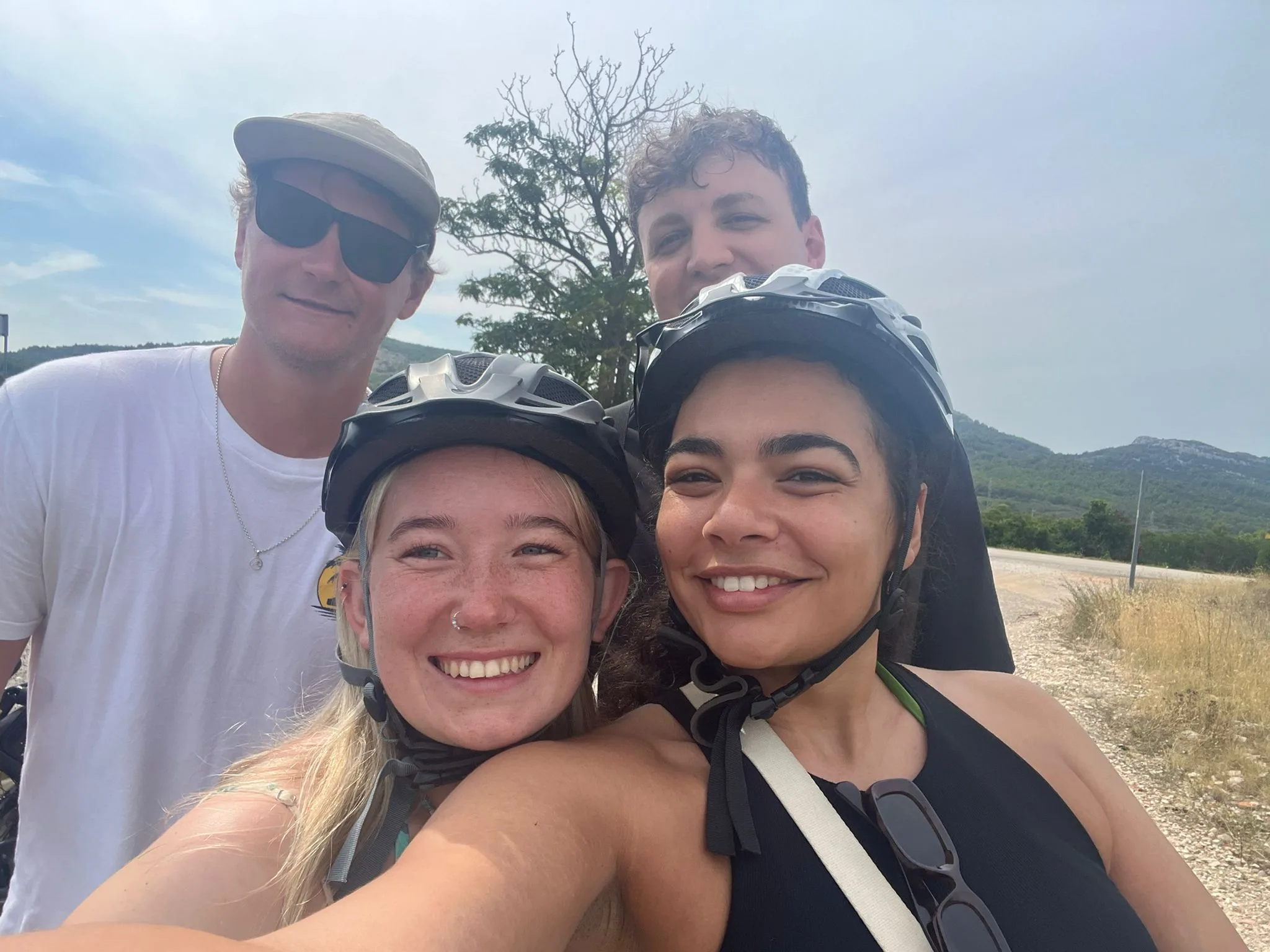 Tessa, Callum and two friends in cycling helmets on a sunny hillside road.