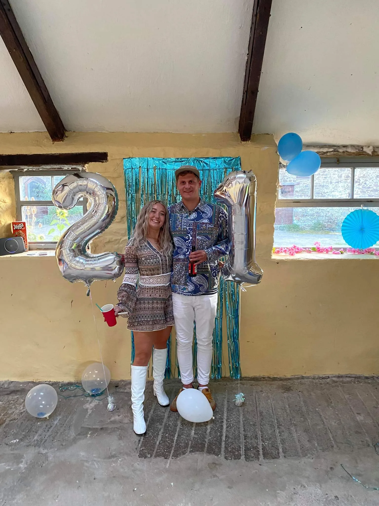 Tessa and Callum dressed up beside giant silver 21 balloons at a birthday party.
